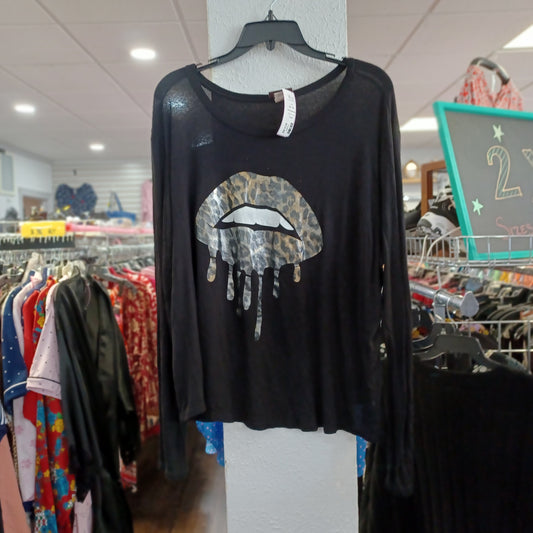 A black long-sleeve top hanging on a hanger in a clothing store, featuring a leopard-print dripping lips graphic on the front.